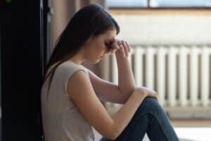 teen sitting against wall hanging head while in need of the benefits of trauma therapy