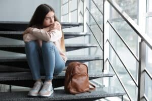 teen sitting on steps hugging knees while showing signs of bipolar disorder